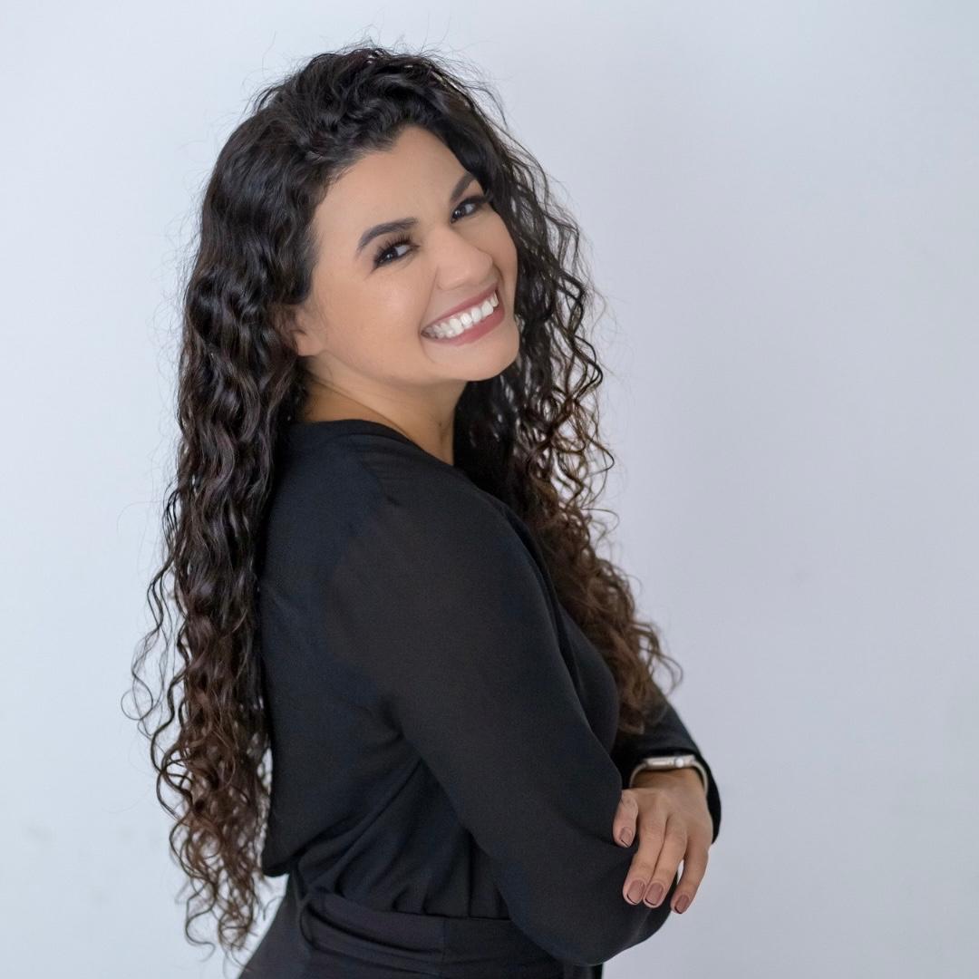 Retrato de Geisy Fernandes sorrindo, de braços cruzados
