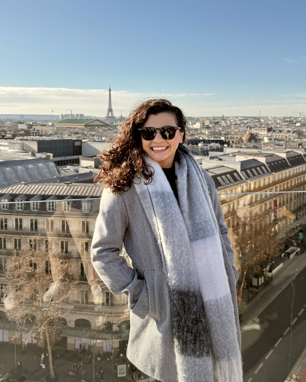 Geisy Fernandes sorrindo de óculos escuros, com a cidade de Paris ao fundo
